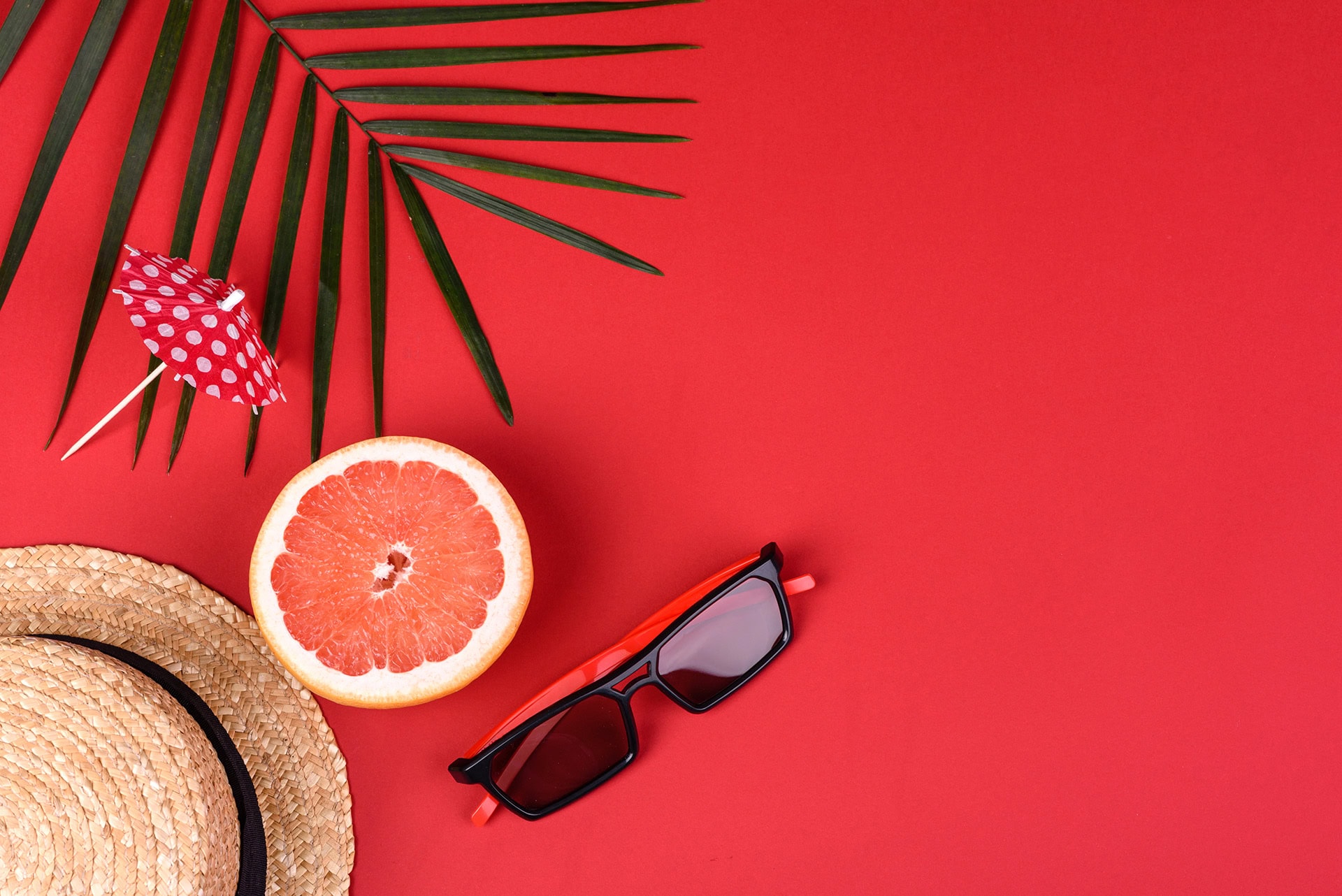 Urlaub und Freizeit: Sonnenbrille, Hut, Grapefruit auf rotem Hintergrund.